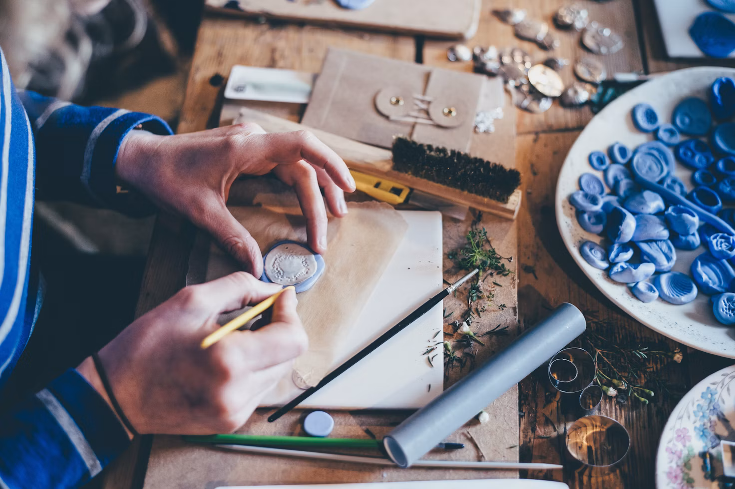 Hands shaping small blue forms at a cluttered workbench